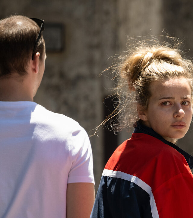 "Kidnapped: The Chloe Ayling Story – Die Ermittlung": Chloe (Nadia Parkes) und MD (Julian Świeżewski) gehen nebeneinander an einem großen Gebäude entlang. Sie schaut sich nach hinten um.
