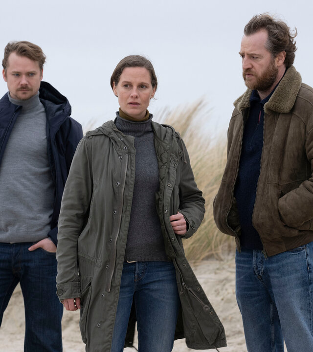 "Ostfriesentotenstille": Kommissarin Ann Kathrin Klaasen (Picco von Groote) steht zusammen mit ihrem Kollegen Frank Weller (Tom Radisch) und Dr. Bernhard Sommerfeldt (Sven Schelker) am Rande einer Düne. Jeder hat einen nachdenklichen und ernsten Blick.