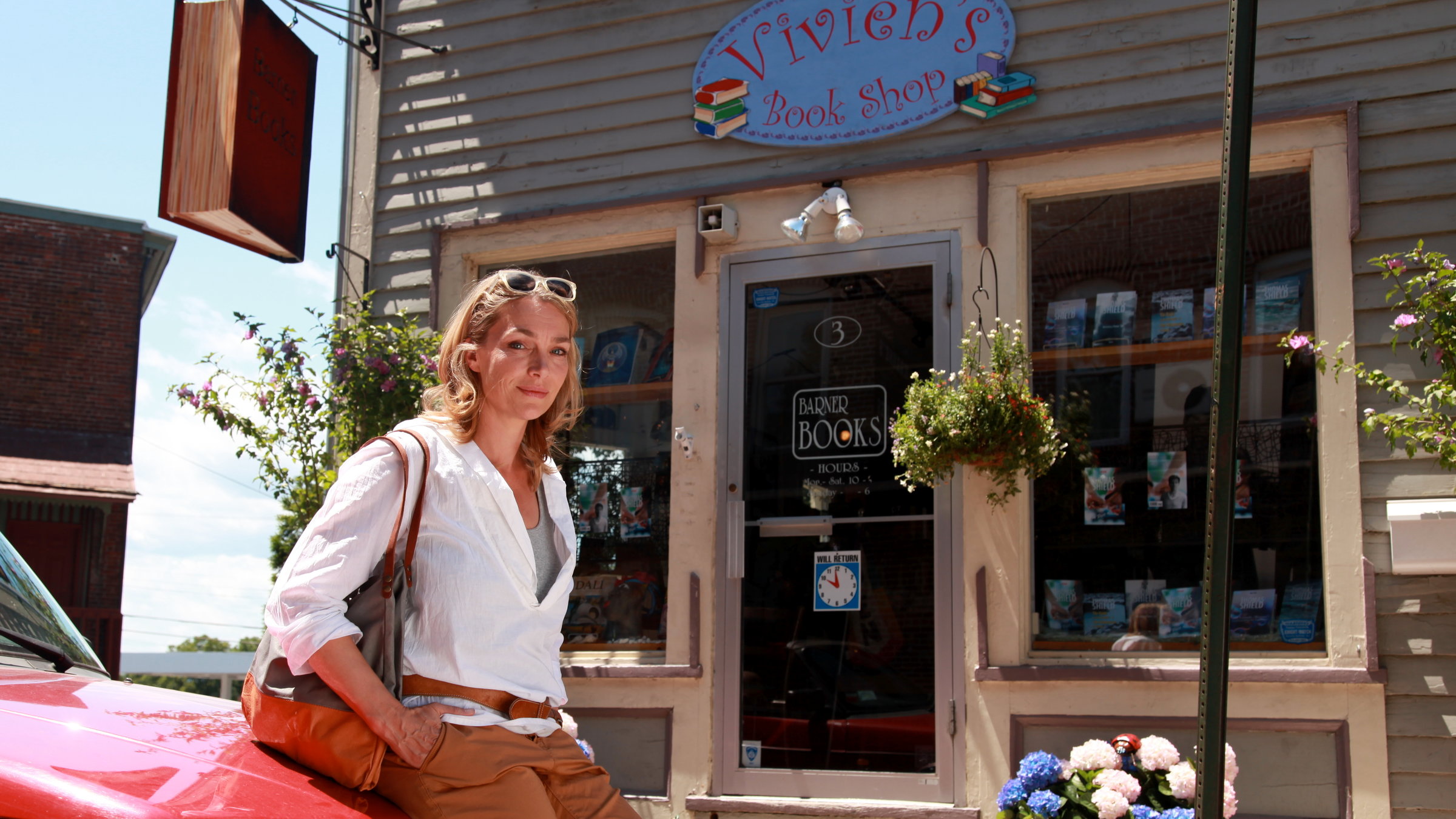 "Katie Fforde: Ein Teil von dir": Vivien Barner (Aglaia Szyszkowitz) steht an ihr Auto gelehnt vor ihrem Buchladen. Sie sieht nachdenklich aus.