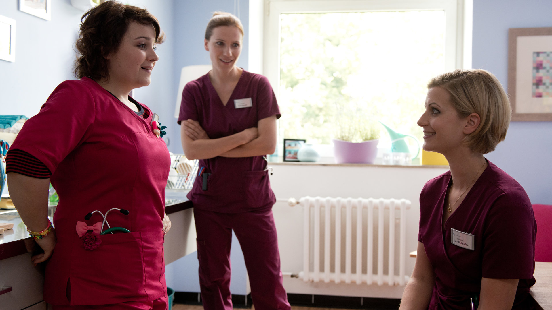 "Bettys Diagnose - Vergeben und Vergessen": Talula (Carolin Walter), Betty (Bettina Lamprecht) und Lizzy (Theresa Underberg) stehen in einer Küche und unterhalten sich lächelnd.