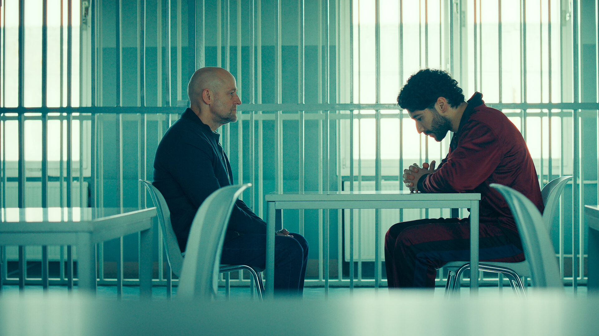 "Jenseits der Spree - Kalkuliertes Risiko": Robert Heffler (JÃ¼rgen Vogel) und Mo Kassem (Mohamed Kanj Khamis) sitzen sich an einem Tisch in einem Besucherraum eines GefÃ¤ngnis' gegenÃ¼ber. Robert Heffler sitzt aufrecht und blickt zu Mo Kassem, der mit nach vorn gebeugtem OberkÃ¶rper am Tisch sitzt und seine HÃ¤nde vor sich gefaltet hat. Im Hintergrund sind vergitterte TrennwÃ¤nde und weitere Tische.
