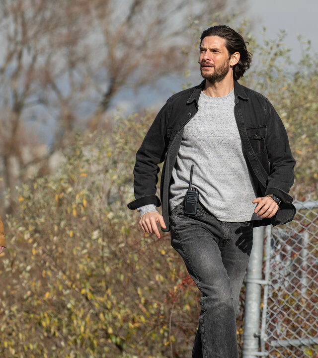 "Das Institut - Die Hölle wartet": Luke (Joe Freeman) und Tim (Ben Barnes) sind im Freien unterwegs. Sie wirken gehetzt. Im Hintergrund blüht ein Busch hinter einem Maschendrahtzaun.