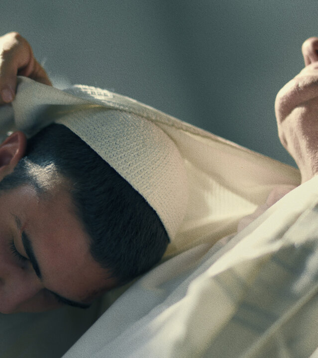 "Borders - Avi Superstar": Avi (Ben Sultan) und Salomon (Shlomi Shabat) sitzen in der Synagoge nebeneinander. Beide tragen Kippa und Tallit. Salomon bedeckt mit seinem Gebetsmantel den Kopf von Avi.