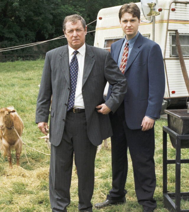 "Inspector Barnaby - Mord auf der Durchreise": DCI Tom Barnaby (John Nettles) und Sergeant Gavin Troy (Daniel Casey) stehen nebeneinander auf einer Wiese vor einem Wohnwagen. Hinter ihnen sind zwei Schafe zu sehen.