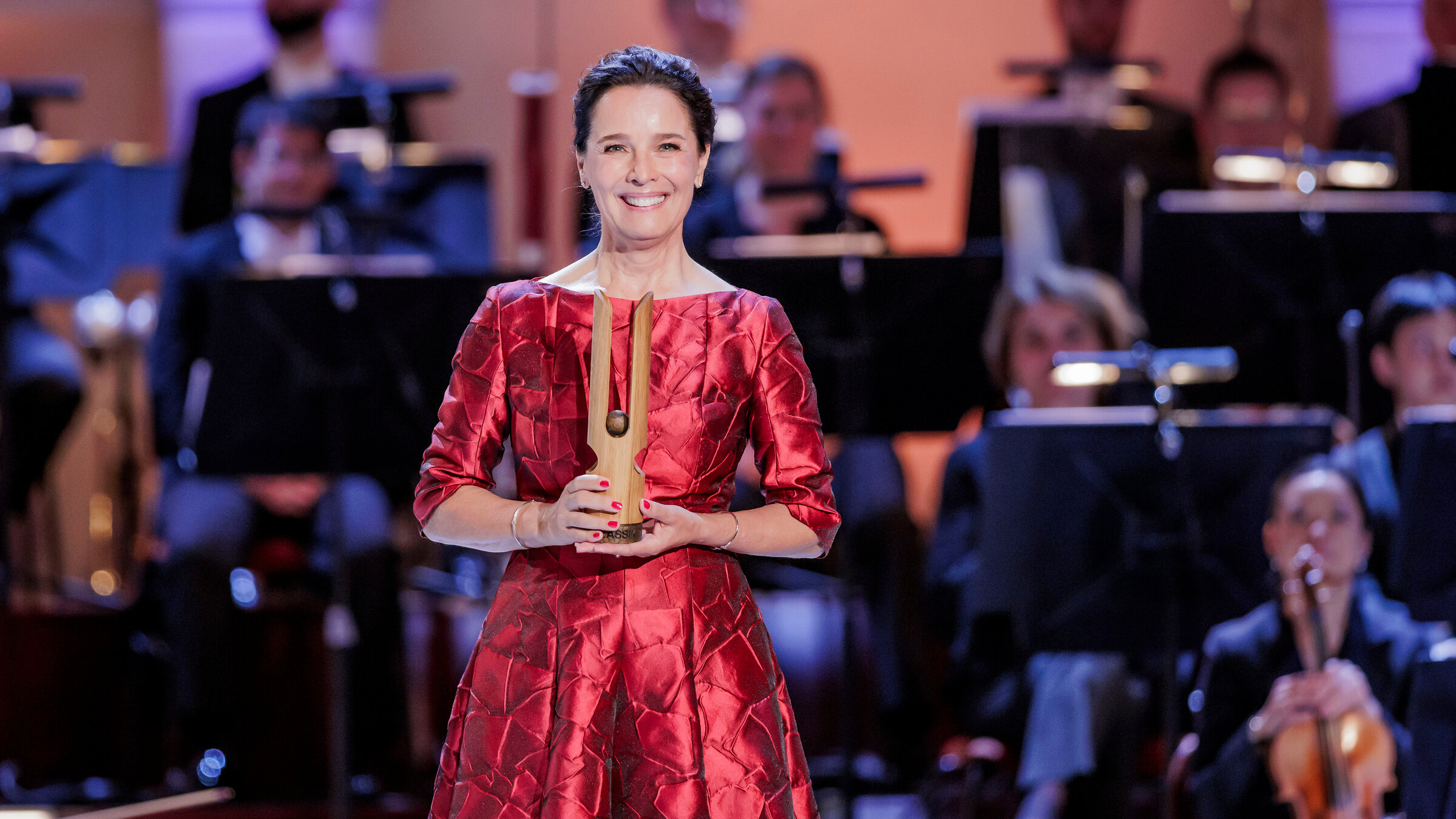 "OPUS KLASSIK 2025": Désirée Nosbusch steht vor einem Orchester.