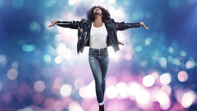 "Whitney Houston: I Wanna Dance With Somebody": Whintney Houston (Naomie Ackie) tanzt mit ausgebreiteten Armen, umhüllt von Lichteffekten.