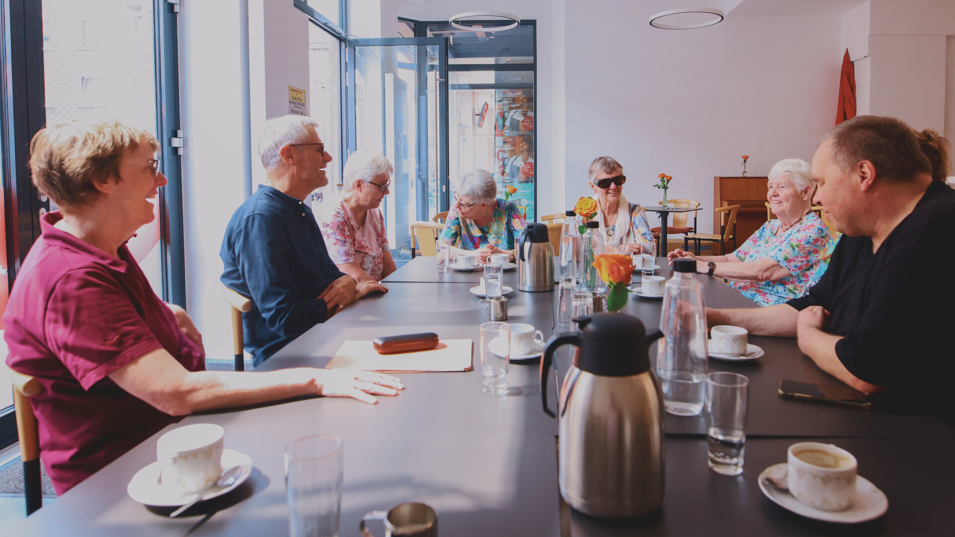 "Aktion Mensch - Glückszahlen der Woche": In dem neu eröffneten, barrierefreien Café sitzen acht Personen um einen Tisch herum.