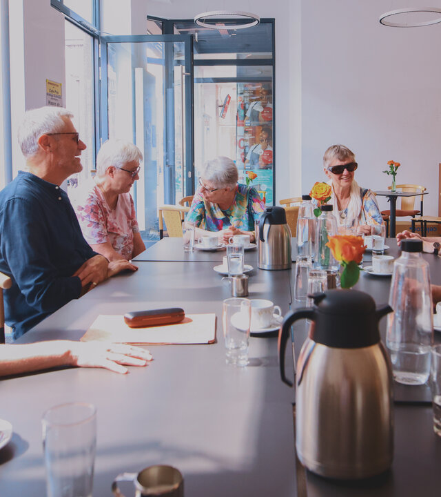"Aktion Mensch - Glückszahlen der Woche": In dem neu eröffneten, barrierefreien Café sitzen acht Personen um einen Tisch herum.