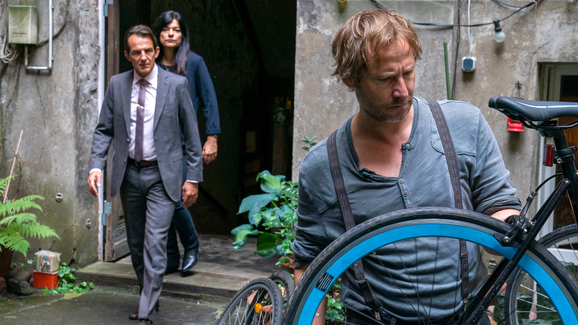 "Letzte Spur Berlin - Doomsday": Oliver Radek (Hans-Werner Meyer) und Mina Amiri (Jasmin Tabatabai) sind auf dem Weg zu Andreas Weiland (Niels Bruno Schmidt), der in einem Innenhof mit dem Rücken zu den beiden steht und ein Fahrrad repariert.