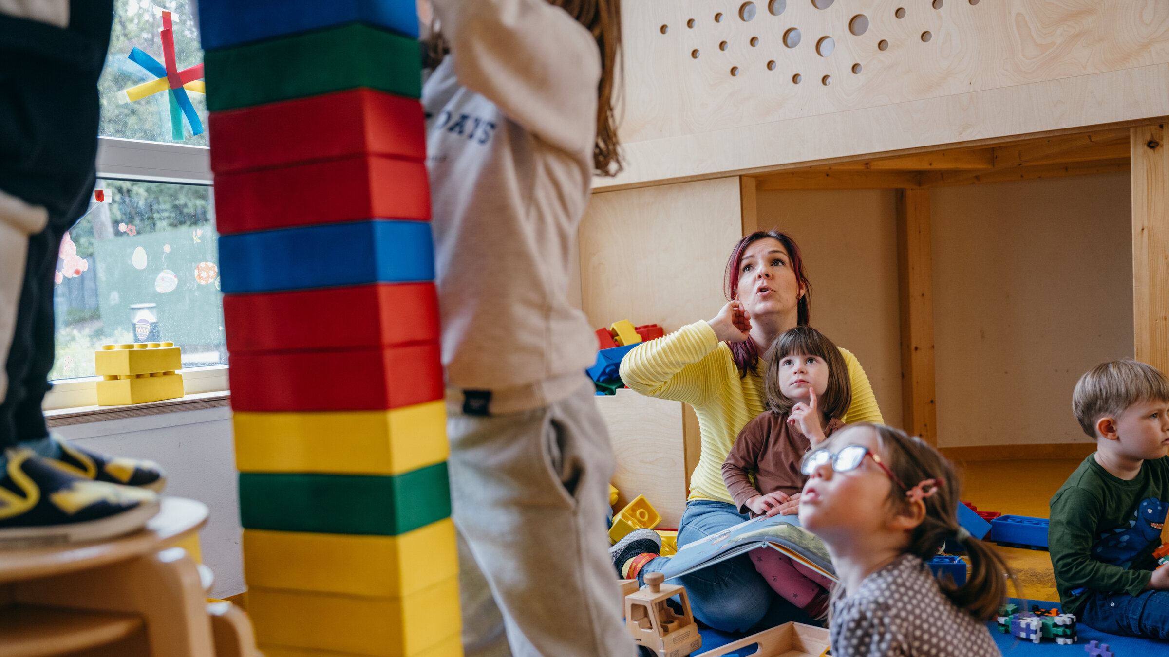 "Kein Kinderspiel! - System Kita am Anschlag": Im Kindergarten: Erzieherin Diana sitzt mit ihren Kindergartenkindern am Boden, zwei Kinder stehen im Vordergrund und bauen einen Turm.