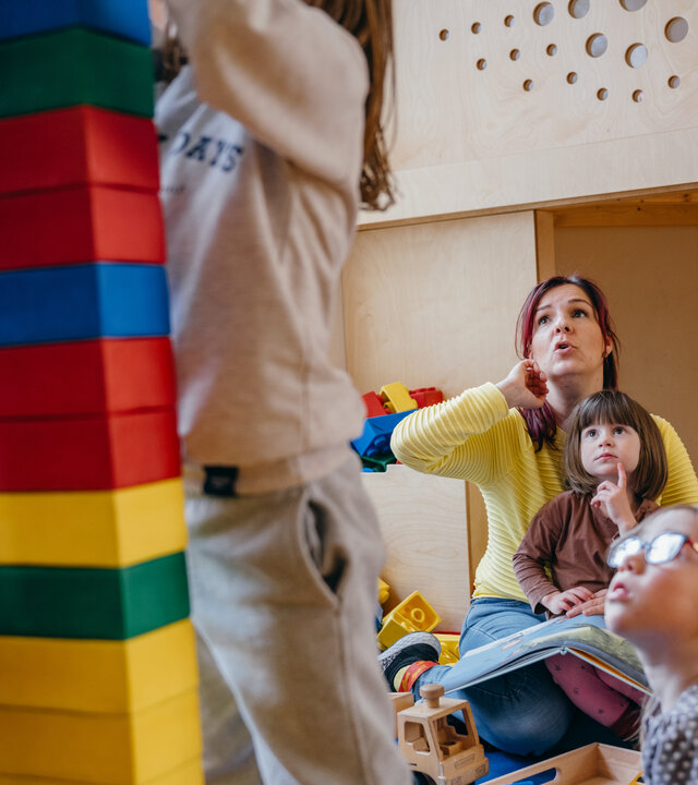 "Kein Kinderspiel! - System Kita am Anschlag": Im Kindergarten: Erzieherin Diana sitzt mit ihren Kindergartenkindern am Boden, zwei Kinder stehen im Vordergrund und bauen einen Turm.