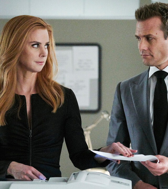 "Suits - Versprechen, nichts als Versprechen": Sarah (Sarah Rafferty) steht neben Harvey (Gabriel Macht) an einem Kopierer und überreicht ihm ein Dokument. Dabei wirft sie ihm einen vielsagenden Blick zu. Im Hintergrund ist ein Regal mit Papierpaketen zu erkennen.