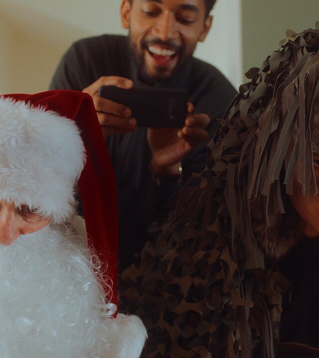 "Doppelhaushälfte - Schöne Bescherung": Andi (Milan Peschel) ist als Weihnachtsmann verkleidet und Rocco (Hoang Minh Ha) als Knecht Ruprecht. Sie schauen nach vorne gebeugt mit intensivem Blick Richtung Kamera. Hinter ihnen steht mich lachendem Blick Theo (Benito Bause) und filmt mit dem Handy das Geschehen.