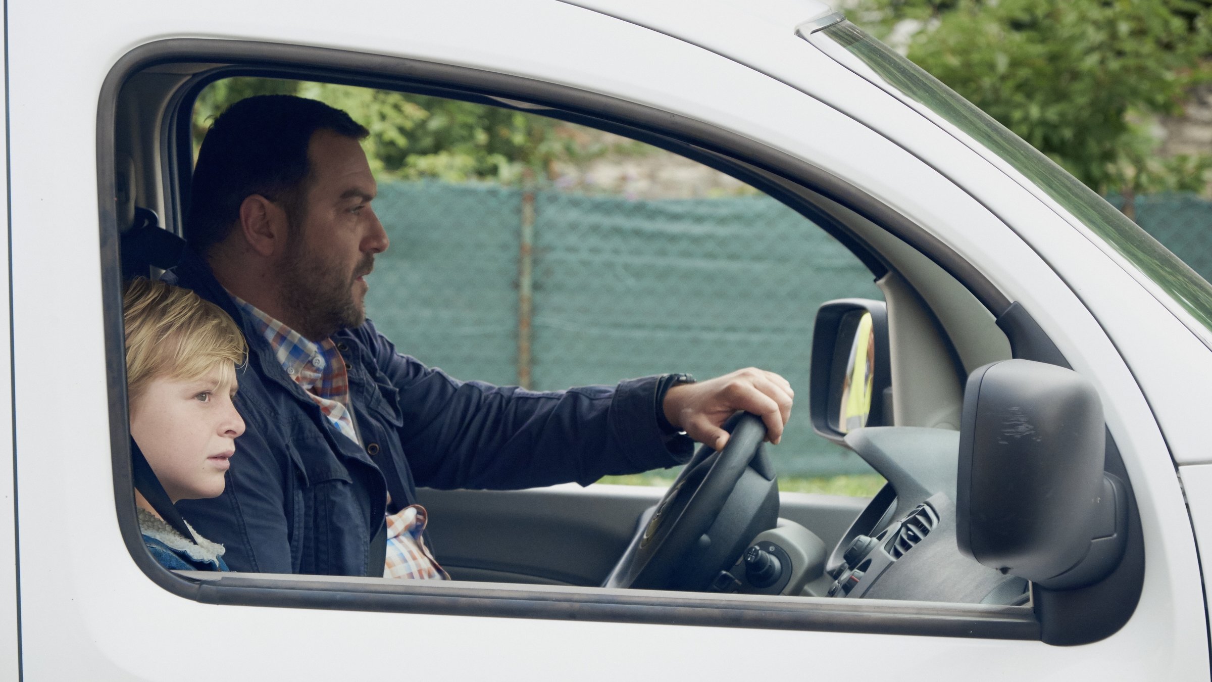 "Nach dem Urteil": Durch das Beifahrerfenster schaut man in ein Auto, in dem ein älterer Mann mit etwas grimmigem Gesichtsausdruck am Lenkrad sitzt. Beifahrer ist ein blondhaariger Junge, von dem man durch den Fensterrahmen nur den angeschnittenen Kopf sieht.
