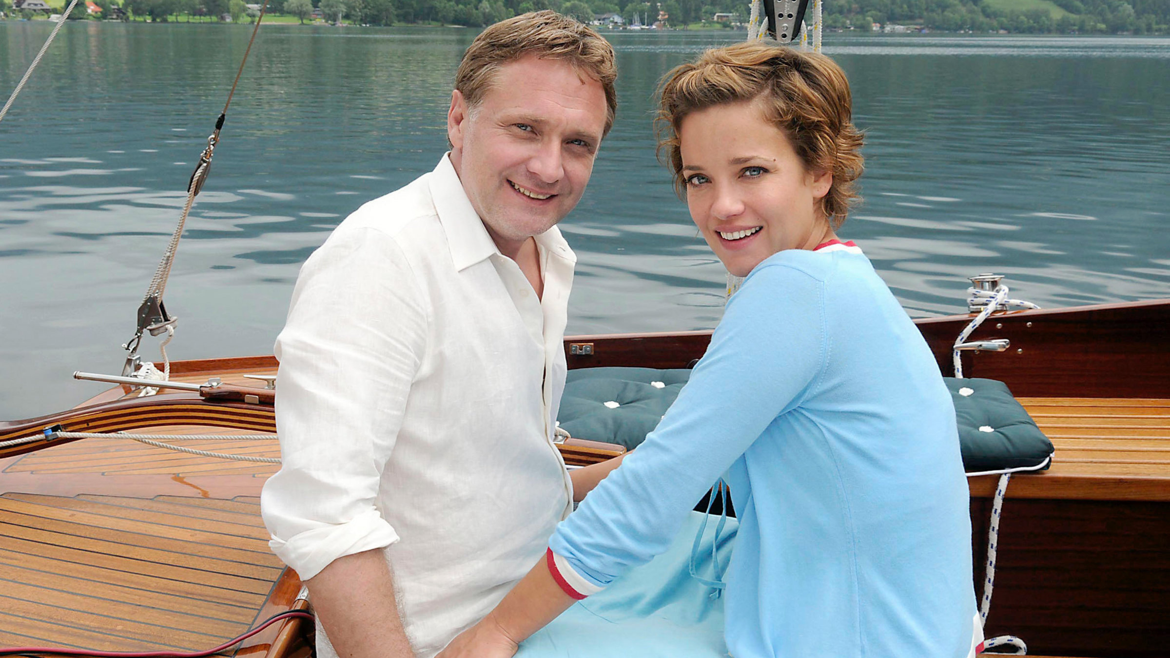 "Lilly Schönauer: Und dann war es Liebe": Phillip (Bernhard Schir) und Jana (Muriel Baumeister) gehen auf Segeltörn. Sie halten sich an den Händen und schauen lächelnd aus dem Bild.