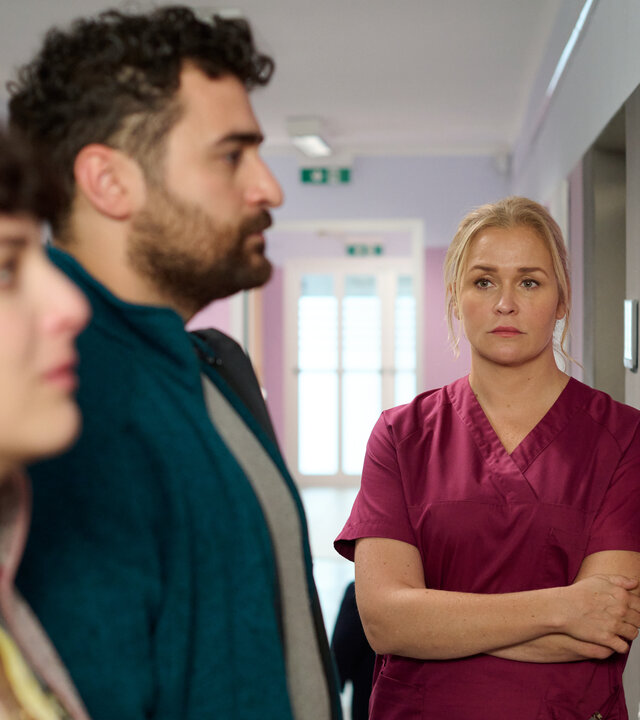 "Lena Lorenz - Das Leben ist jetzt": In einem Krankenhausflur stehen Ina (Anna Werner Friedmann) und Felipe Fromme (Ugur Kaya) vor einer Pinwand mit Babyfotos, die sie mit verzweifeltem Gesichtsausdruck betrachten. Lena Lorenz (Judith Hoersch) steht mit verschränkten Armen daneben und schaut das Paar traurig an.