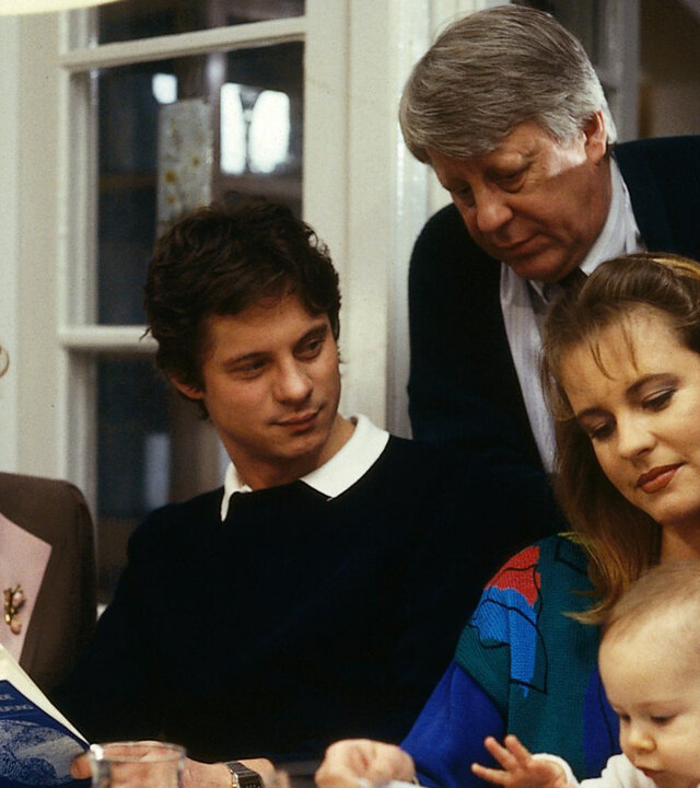 "Die Wicherts von nebenan: Heinz in der Klemme": Oma Käthe (Edith Schollwer), Rüdiger (Jochen Schroeder) und Uschi (Anja Schüte) sitzen am Tisch. Uschi hat Baby Katharina auf ihrem Schoß. Hinter ihr steht Eberhard (Stefan Orlac). Rüdiger hält ein Buch in der Hand.