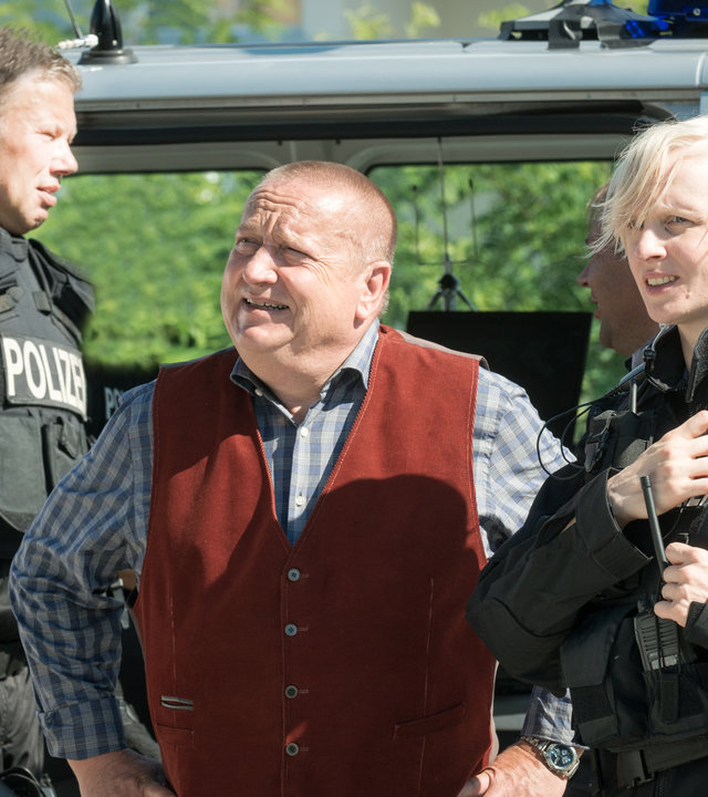 "SOKO Wismar – Überfall!": Revierchef Reuter (Udo Kroschwald) steht zwischen einem SEK-Kollegen (Komparse) und der uniformierten SEK-Beamtin Elke Brandt (Anne Müller) vor einem blauen Polizeibus.