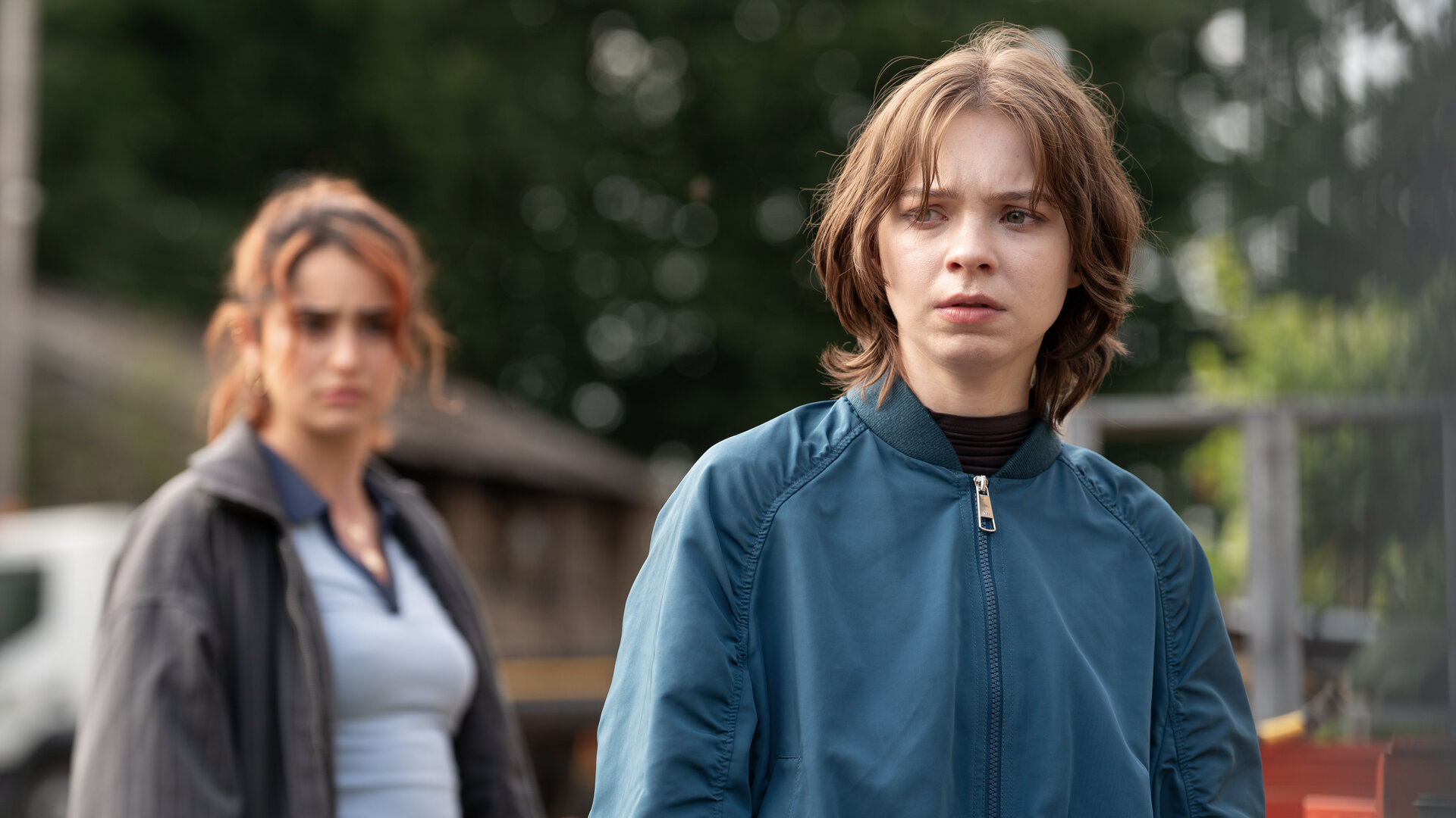 "A Good Girl’s Guide to Murder – Ot Alyal, evol Eimaj": Pip Fitz-Amobi (Emma Myers) steht mit ernstem, fokussiertem Blick während der Suchaktion nach Jamie im Freien. Naomi Ward (Yasmin Al-Khudhairi) steht seitlich hinter ihr und beobachtet Pip besorgt.