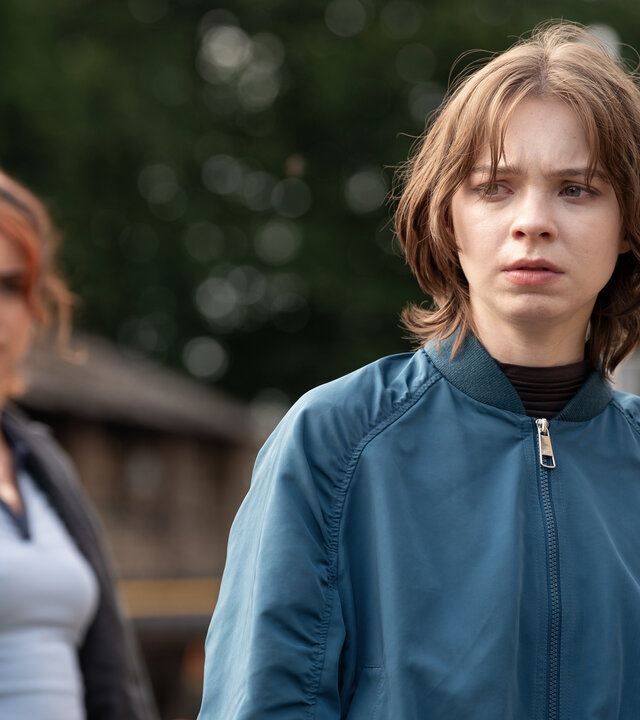 "A Good Girl’s Guide to Murder – Ot Alyal, evol Eimaj": Pip Fitz-Amobi (Emma Myers) steht mit ernstem, fokussiertem Blick während der Suchaktion nach Jamie im Freien. Naomi Ward (Yasmin Al-Khudhairi) steht seitlich hinter ihr und beobachtet Pip besorgt.