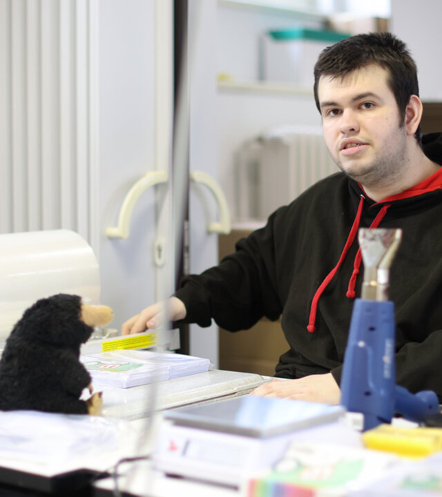 "einfach Mensch - Jan Heinrich Schulze: Durchstarten im Beruf!": Jan Heinrich Schulze (20) sitzt im Büro an seinem Arbeitsplatz und schaut in die Kamera.