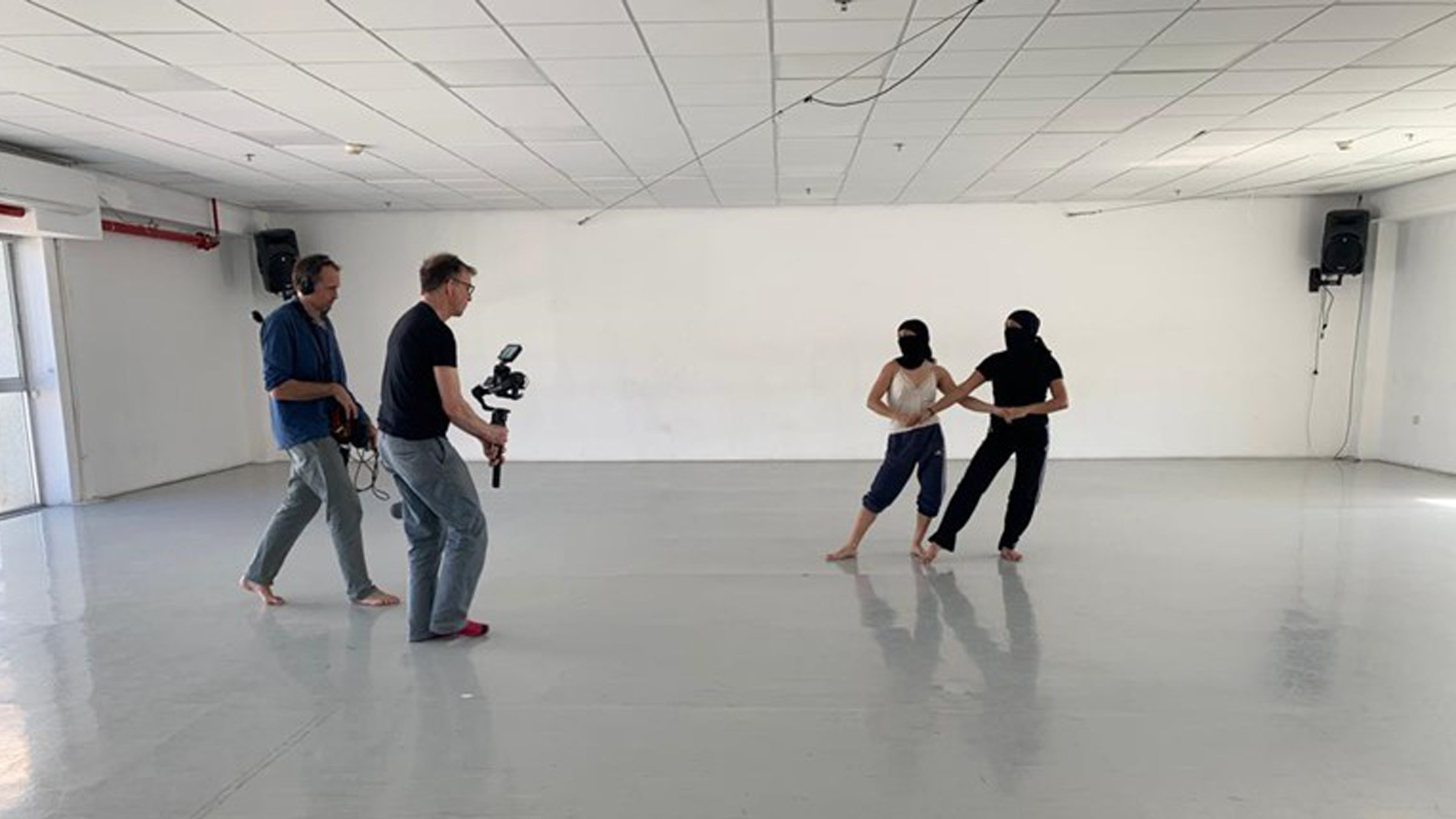 "Tanz aus Israel": Zwei Tänzer in einem nüchternen Probenraum. Die Tänzer haben schwarze Tücher vor dem Gesicht. Nur die Augen sind erkennbar. Sie stehen nebeneinander und halten sich an den Händen. Vor ihnen steht ein Kamera- und ein Ton-Mann.