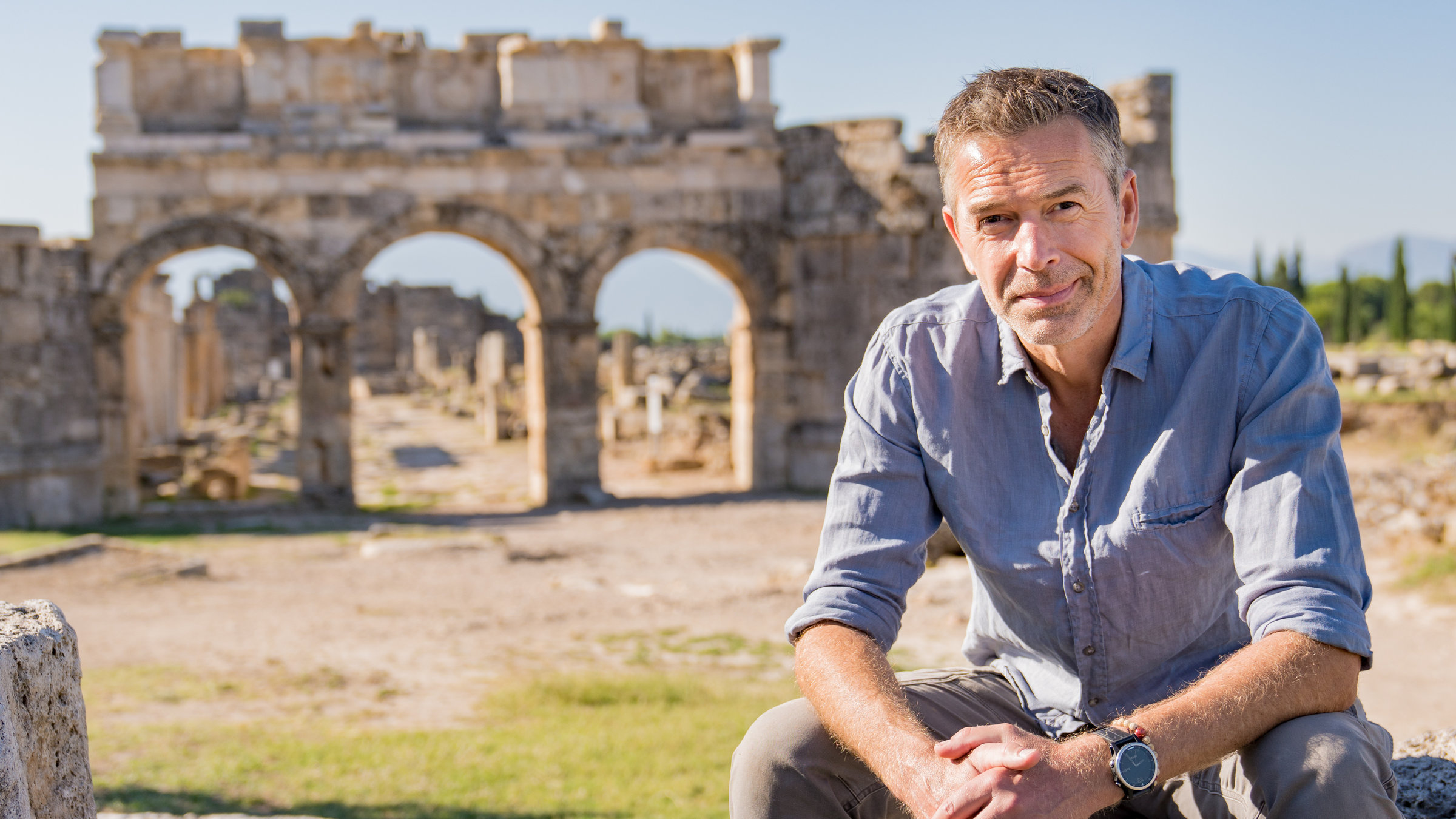 "Terra X: Rätselhafte Phänomene - Sternengold und der Hauch des Todes": Dirk Steffens sitzt auf einem Stein im Amphitheater von Hierapolis in der Türkei und schaut in die Kamera.