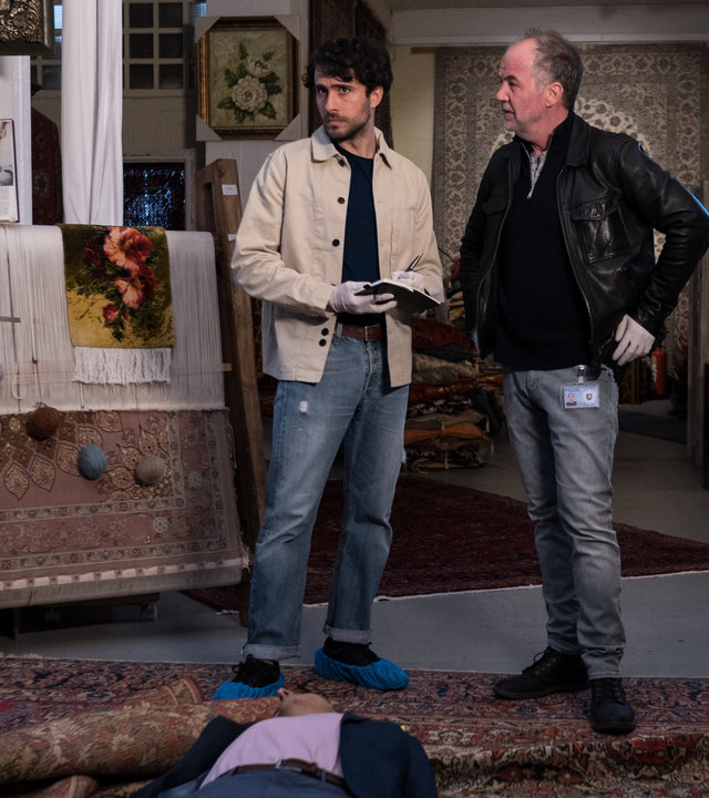 "SOKO Hamburg - Tod eines Teppichhändlers": Max Nordmann (Garry Fischmann) und Oskar Schütz (Marek Erhardt) stehen in einem Teppichladen. Vor ihnen auf dem Boden liegt der tote Farzad Haleh (Yasar Cetin). Max Nordmann hält ein schwarzes Notizbuch in der Hand. Die Kommissare tragen beide weiße Gummihandschuhe.