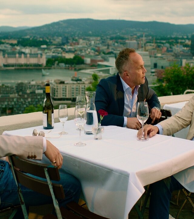 "Exit - Family first": Adam (Simon J. Berger), Jeppe (Jon Øigarden) und Henrik (Tobias Santelmann) sitzen niedergeschlagen an einem Restauranttisch im Freien. Auf dem Tisch stehen eine Flasche Wein und Weingläser.