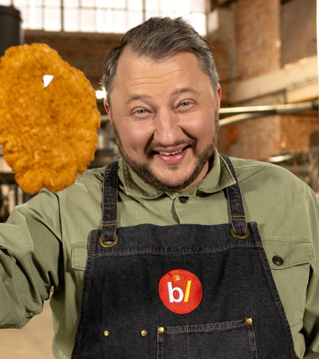"ZDFbesseresser: Die Tricks der deutschen Restaurants - Sebastian Lege deckt auf": Produktentwickler Sebastian Lege hält ein paniertes Schnitzel hoch, das er auf ein Messer gespießt hat.