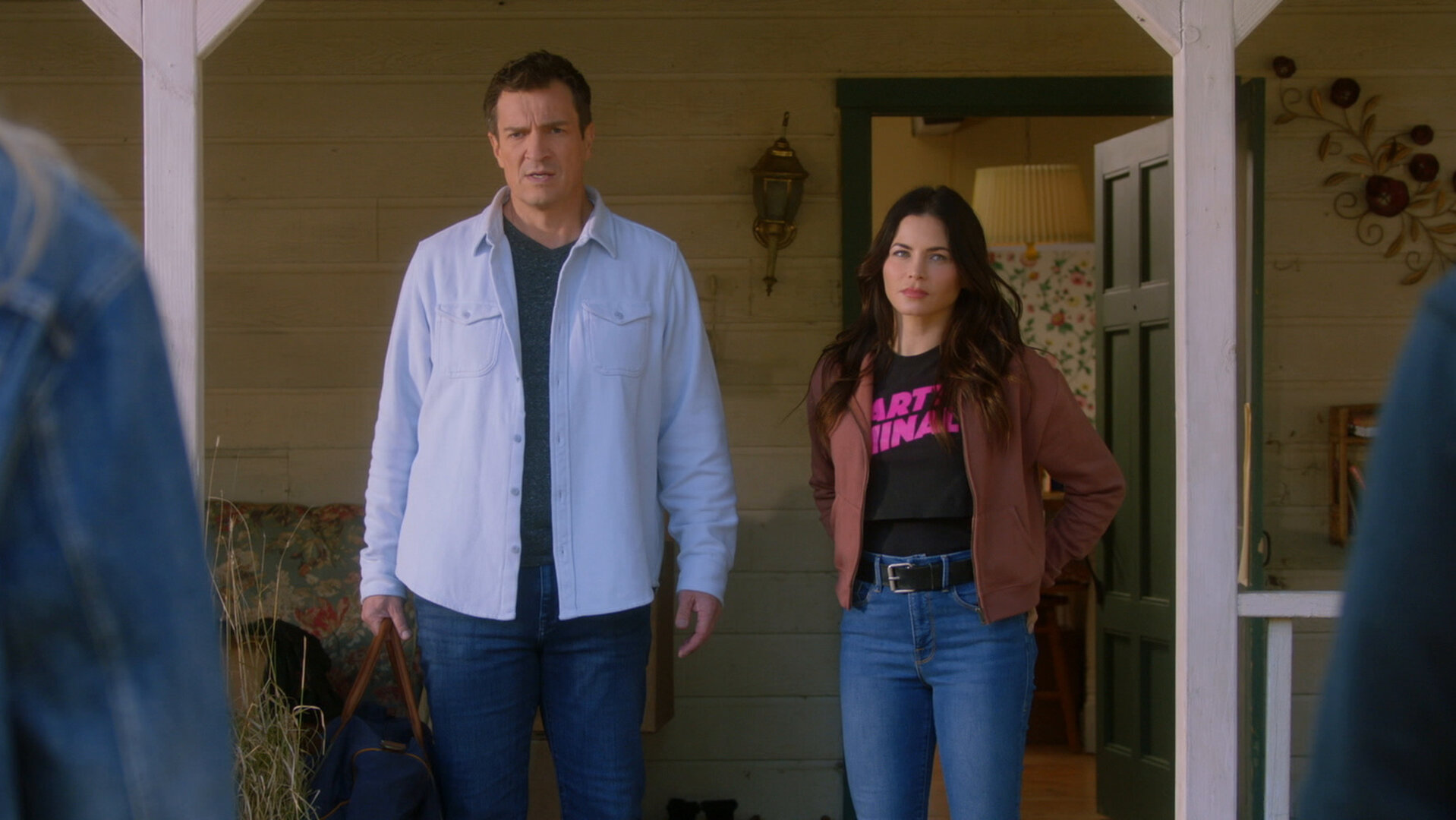 "The Rookie - Die Falle": John Nolan (Nathan Fillion) und Bailey (Jenna Dewan) stehen auf der Veranda des Hauses und betrachten ihre Besucher skeptisch.