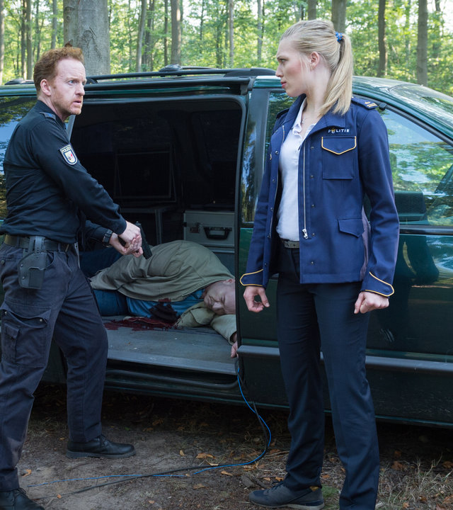 „SOKO Wismar – Verblitzt“: Timmermann (Mathias Junge) steht mit gezogener Waffe vor einem Auto mit geöffneter Tür. Im Wagen liegt ein toter Mann. Anneke van der Meer (Isabel Berghout) steht daneben und sieht ihn an.