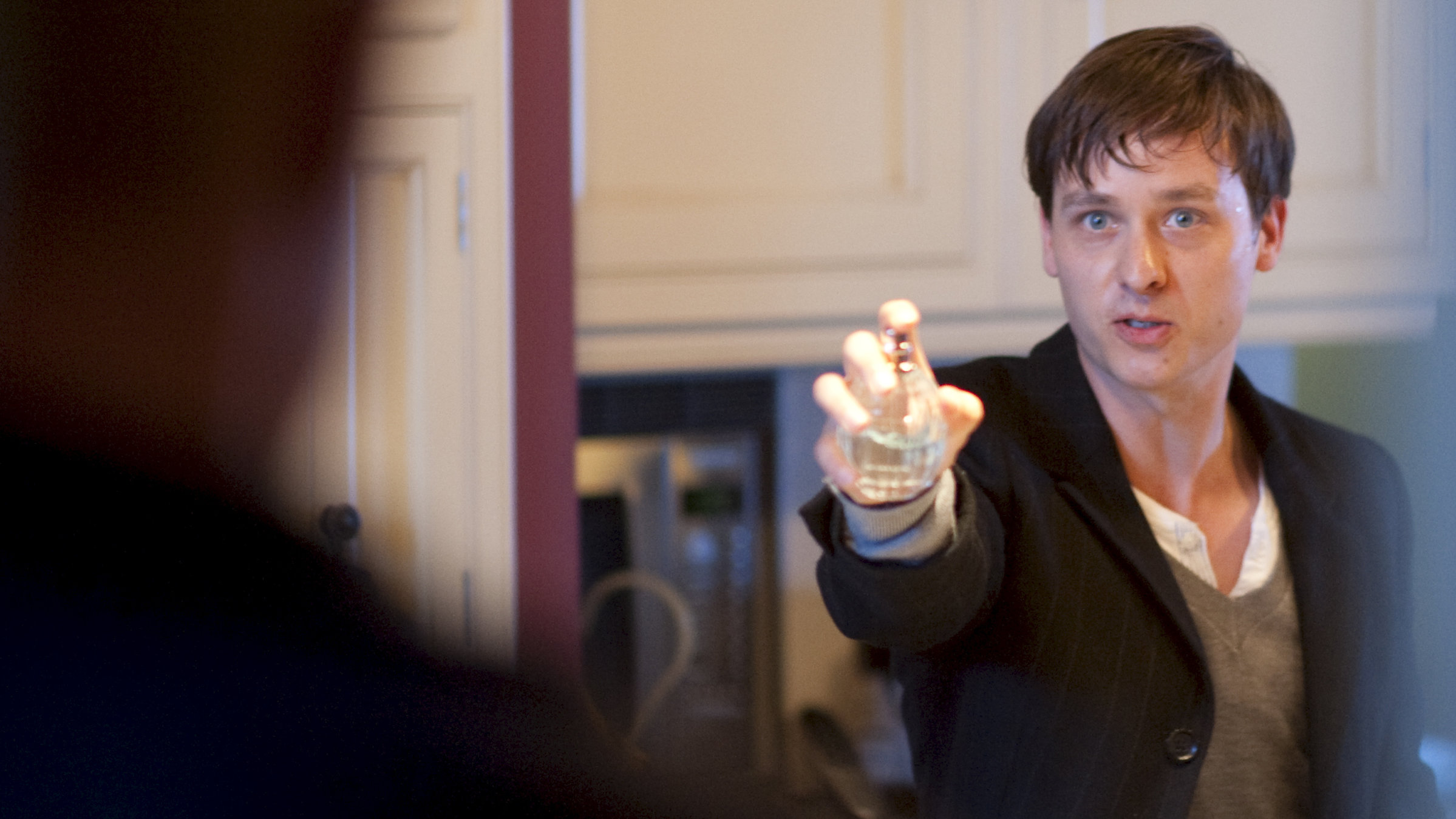 "Ken Follets Eisfieber - Teil 2": Kit (Tom Schilling) streckt seinen Arm nach vorn. In seiner Hand hält er ein kleines Fläschchen mit einem Zerstäuber, auf dem sein Finger liegt. Er schaut nach vorn, wo unscharf die Silhouette einer Person zu erkennen ist.