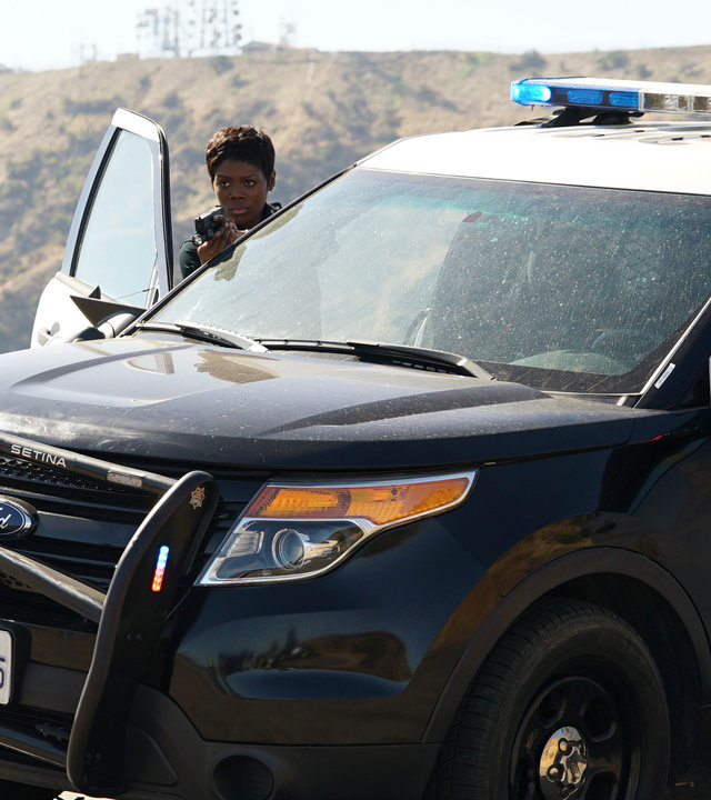 "The Rookie - Crashkurs": John Nolan (Nathan Fillion) und Talia Bishop (Afton Williamson) stehen auf den Hügeln von Los Angeles neben ihrem Polizeiauto und richten ihre Pistolen auf jemanden, den man im Bild nicht sieht. Im Hintergrund der berühmte Hollywood-Schriftzug auf einem der Bergrücken.