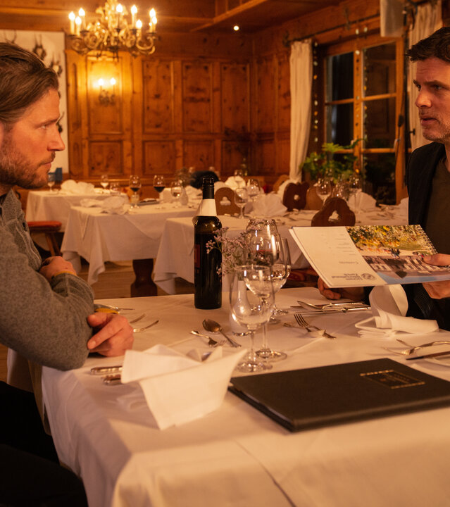 "Die Bergretter: Eiskalte Wahrheit (2)": Markus (Sebastian Ströbel) und Lorenz (Steffen Groth) sitzen mit ernster Miene am gedeckten Tisch im Restaurant.