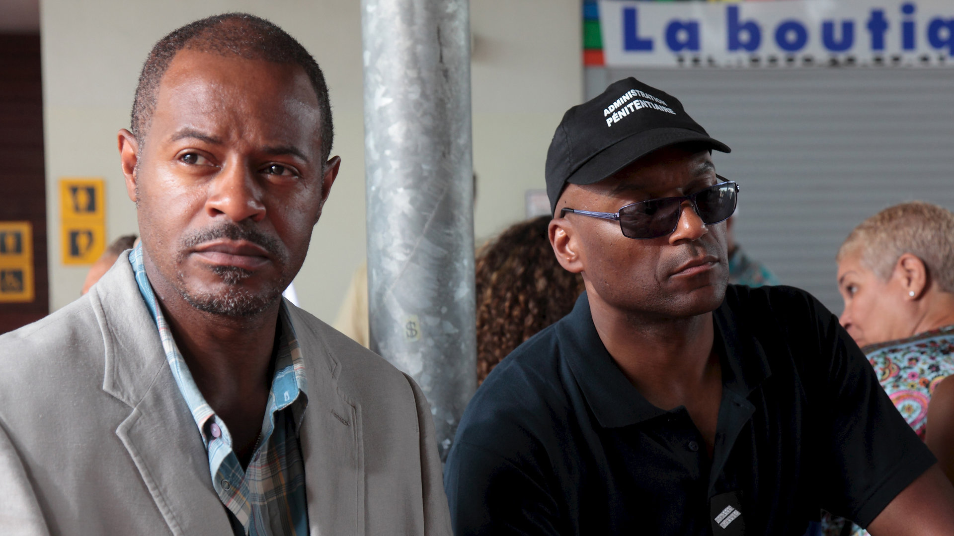 "Death in Paradise - Mord an Bord": Leon Hamilton (Jeff Alexander) und der Gefangene Vincent Carter (Colin Salmon) sitzen in einem Wartebereich.