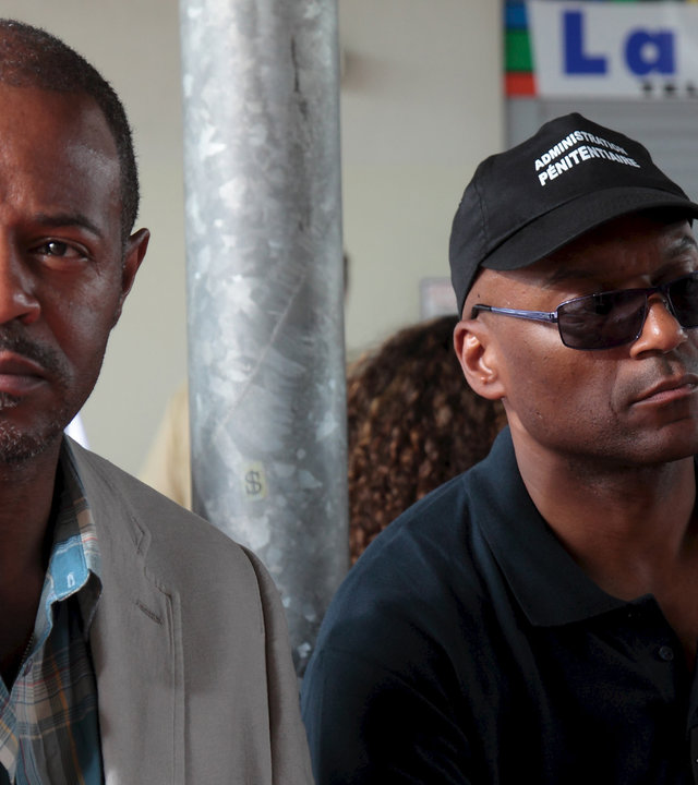 "Death in Paradise - Mord an Bord": Leon Hamilton (Jeff Alexander) und der Gefangene Vincent Carter (Colin Salmon) sitzen in einem Wartebereich.