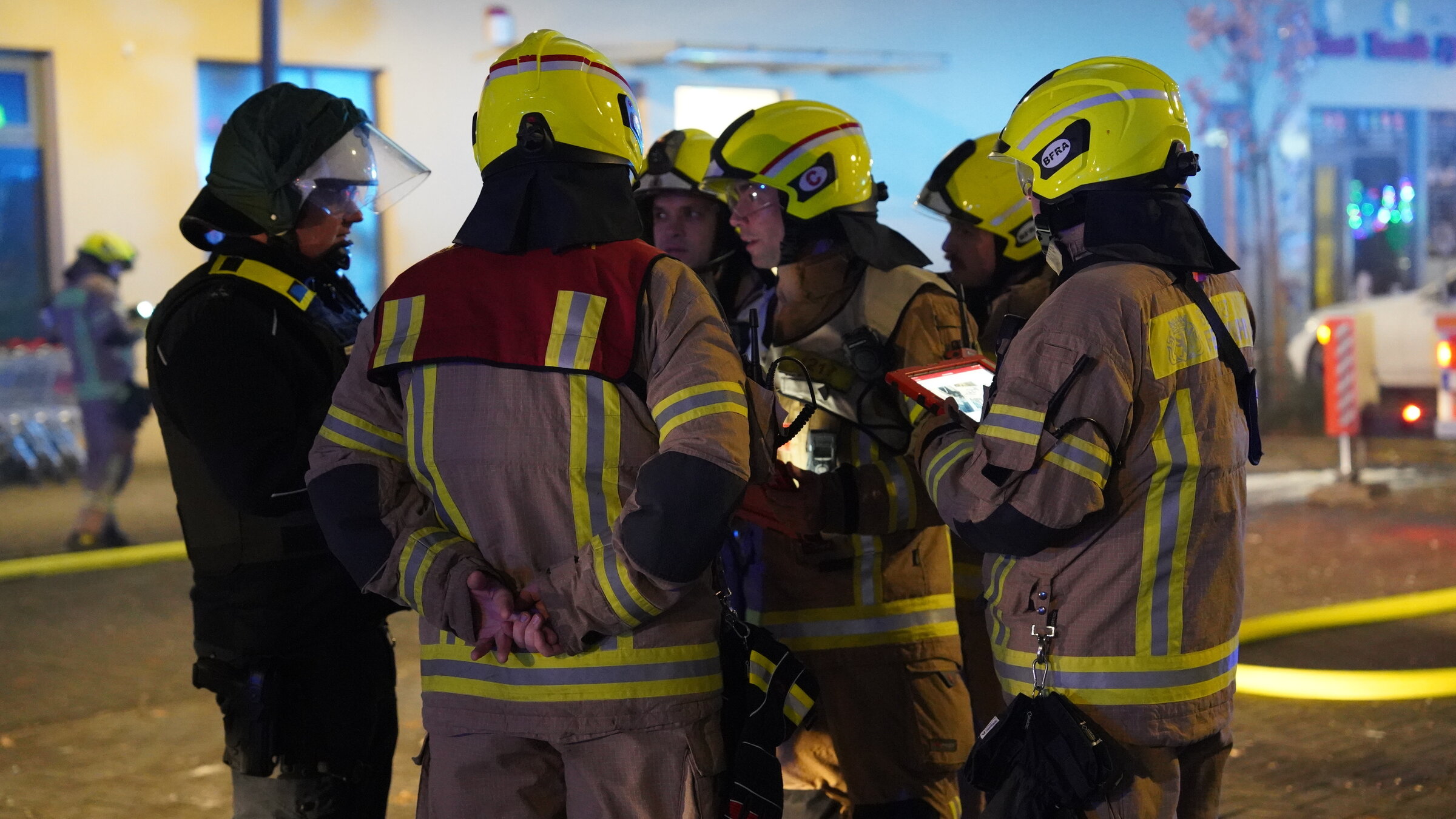 "Wenn Helfen gefährlich wird - Einsatzkräfte in Not": Mehrere Feuerwehrleute stehen bei einem Einsatz in einer urbanen Umgebung eng zusammen.