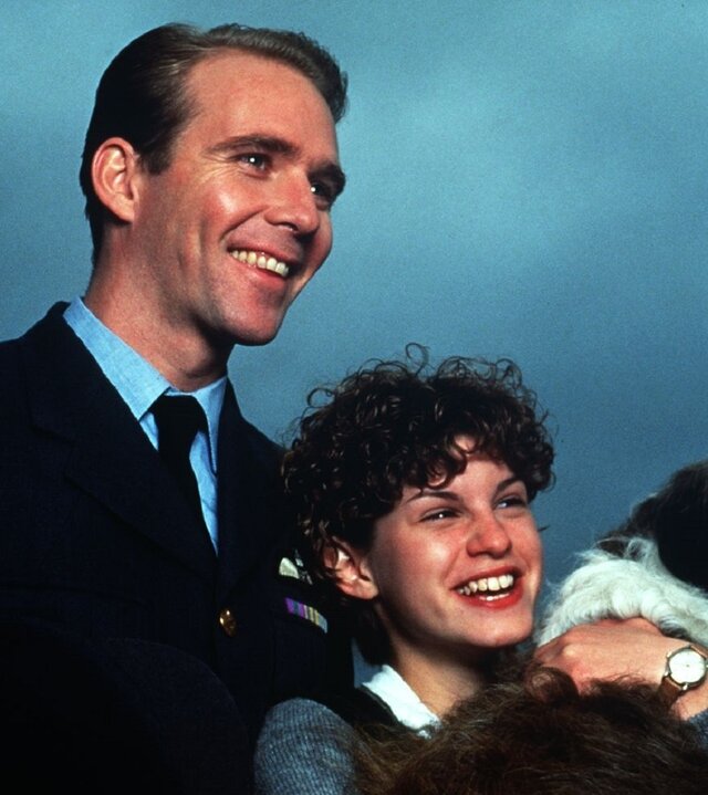 "Fünf Freunde als Retter in der Not": Jeff Thomas (Jason Connery) steht hinter George (Jemima Rooper), die den Hund Timmy im Arm hält. Jeff Thomas (Jason Connery) hat seine rechte Hand auf Georges Arm gelegt. Die beiden lachen und schauen zur Seite.