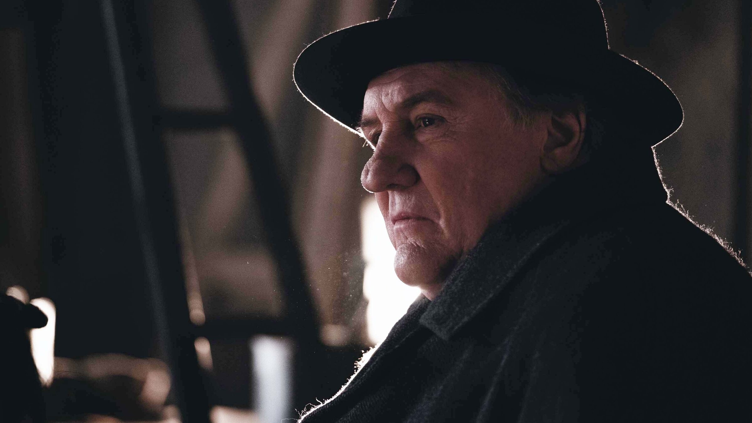 "Maigret und das tote Mädchen": Nahaufnahme: Maigret (Gérard Depardieu) trägt einen dunklen Mantel mit dunklen Hut und blickt nachdenklich und skeptisch zur Seite.