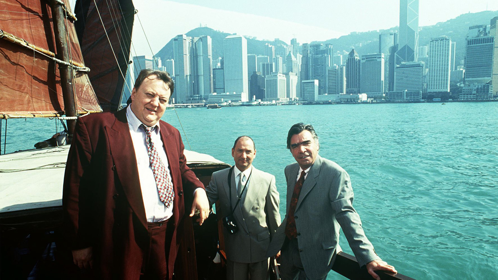 "Das Traumschiff - Hongkong": Auf einem Segelboot stehen Eberhard Meyhopf (Joachim Kemmer), Berthold Böhme (Heinz Rennhack) und Baudezernent Walter Muck (Dieter Pfaff). Im Hintergrund ist die Skyline Hongkongs zu sehen.