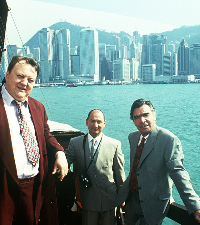 "Das Traumschiff - Hongkong": Auf einem Segelboot stehen Eberhard Meyhopf (Joachim Kemmer), Berthold Böhme (Heinz Rennhack) und Baudezernent Walter Muck (Dieter Pfaff). Im Hintergrund ist die Skyline Hongkongs zu sehen.