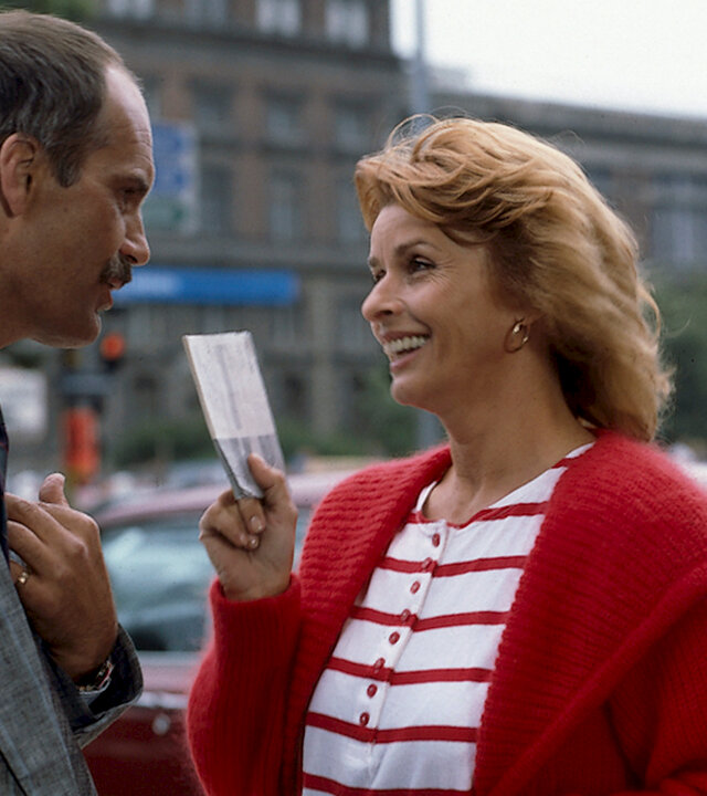 "Die schnelle Gerdi - 6. Miss Miramare": Gerdi unterhält sich lachend mit dem angeblichen Herrn von Wallerstein (Christoph Lindert) auf einem Parkplatz.