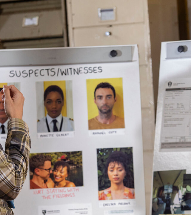 "Death in Paradise - In Luft aufgelöst": DI Neville Parker (Ralf Little) steht nachdenklich vor einer Ermittlungswand mit Fotos von Verdächtigen, Zeugen und dem Opfer, während er zur Seite blickt.