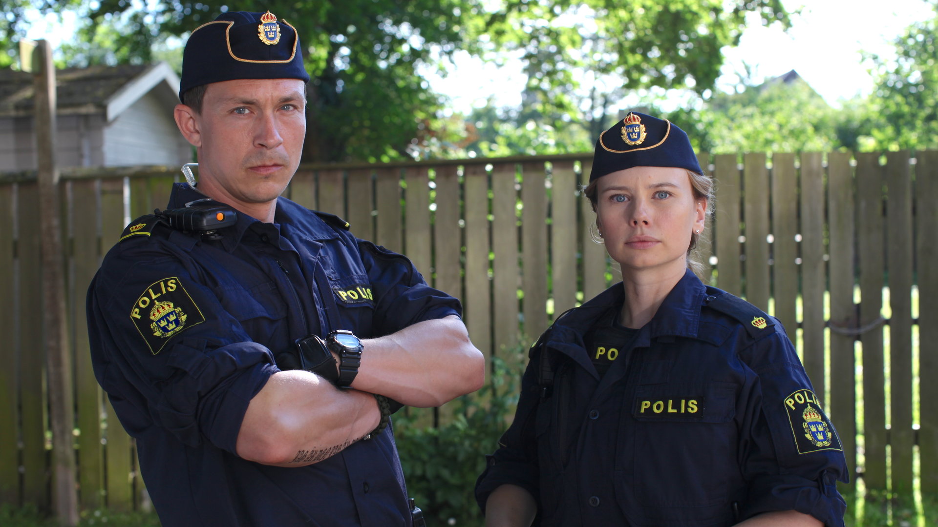 "Thin Blue Line - Eskalation": Magnus (Oscar Töringe) und Sara (Amanda Jansson) stehen nebeneinander vor einem Holzzaun und blicken direkt in Richtung Kamera.