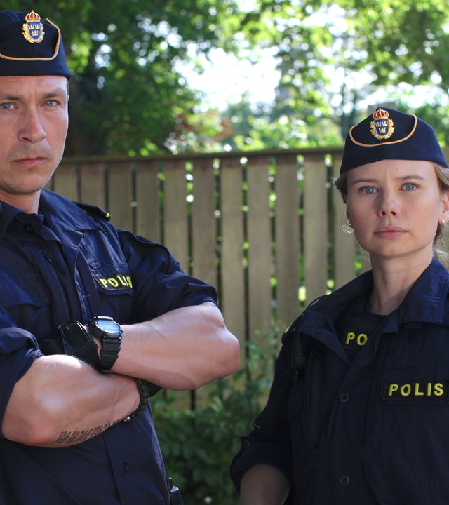 "Thin Blue Line - Eskalation": Magnus (Oscar Töringe) und Sara (Amanda Jansson) stehen nebeneinander vor einem Holzzaun und blicken direkt in Richtung Kamera.