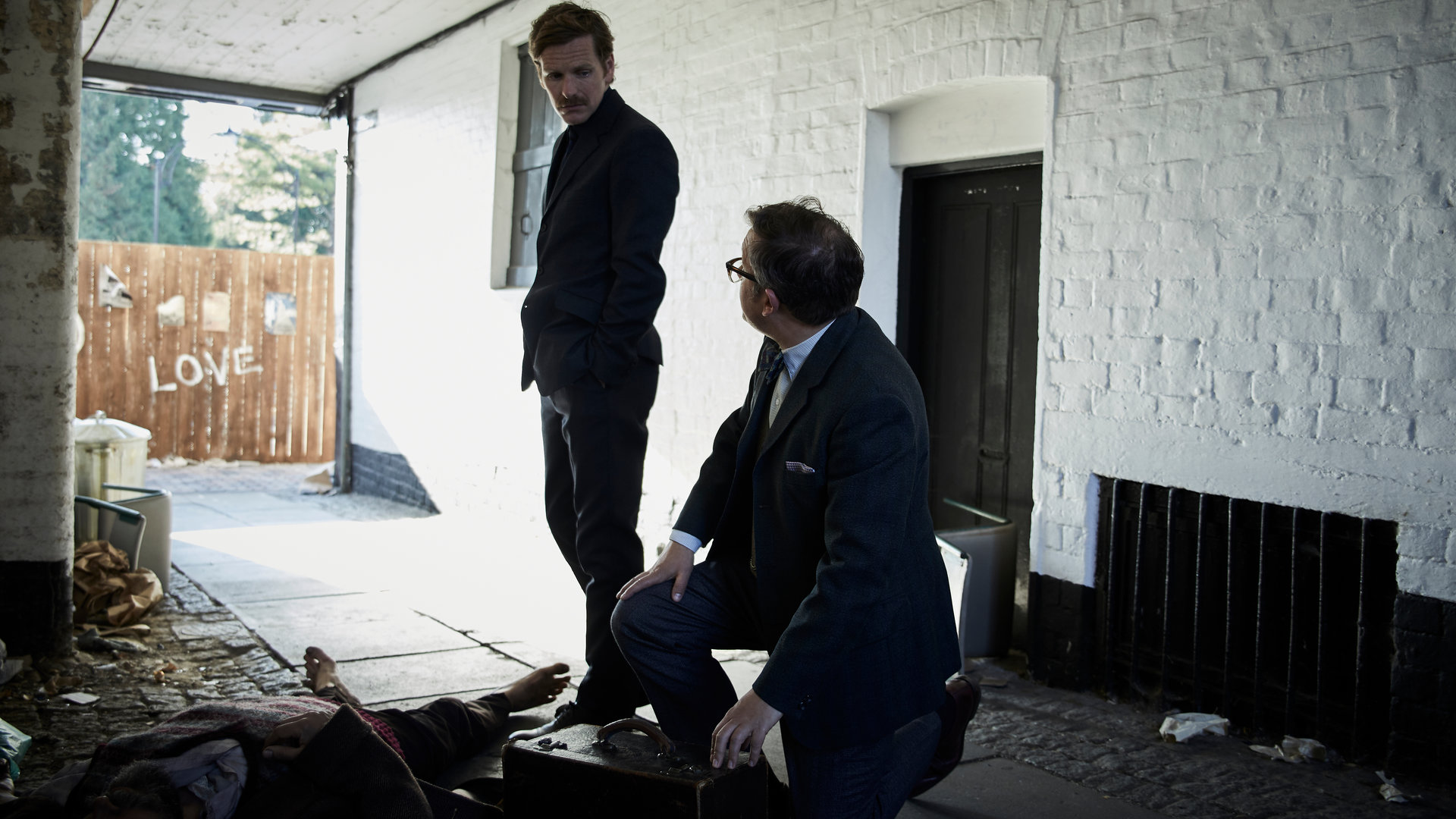 "Der junge Inspektor Morse - Zuckerguss": Dr. Max Derbryn (James Breadshaw) kniet auf dem Boden neben einer Leiche. Endeavour (Shaun Evans) steht daneben und schaut zu Max.
