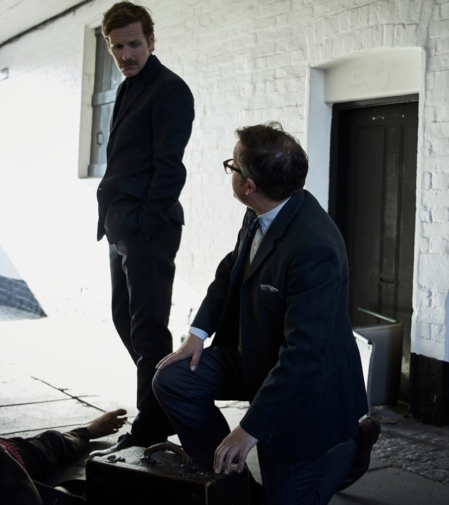 "Der junge Inspektor Morse - Zuckerguss": Dr. Max Derbryn (James Breadshaw) kniet auf dem Boden neben einer Leiche. Endeavour (Shaun Evans) steht daneben und schaut zu Max.