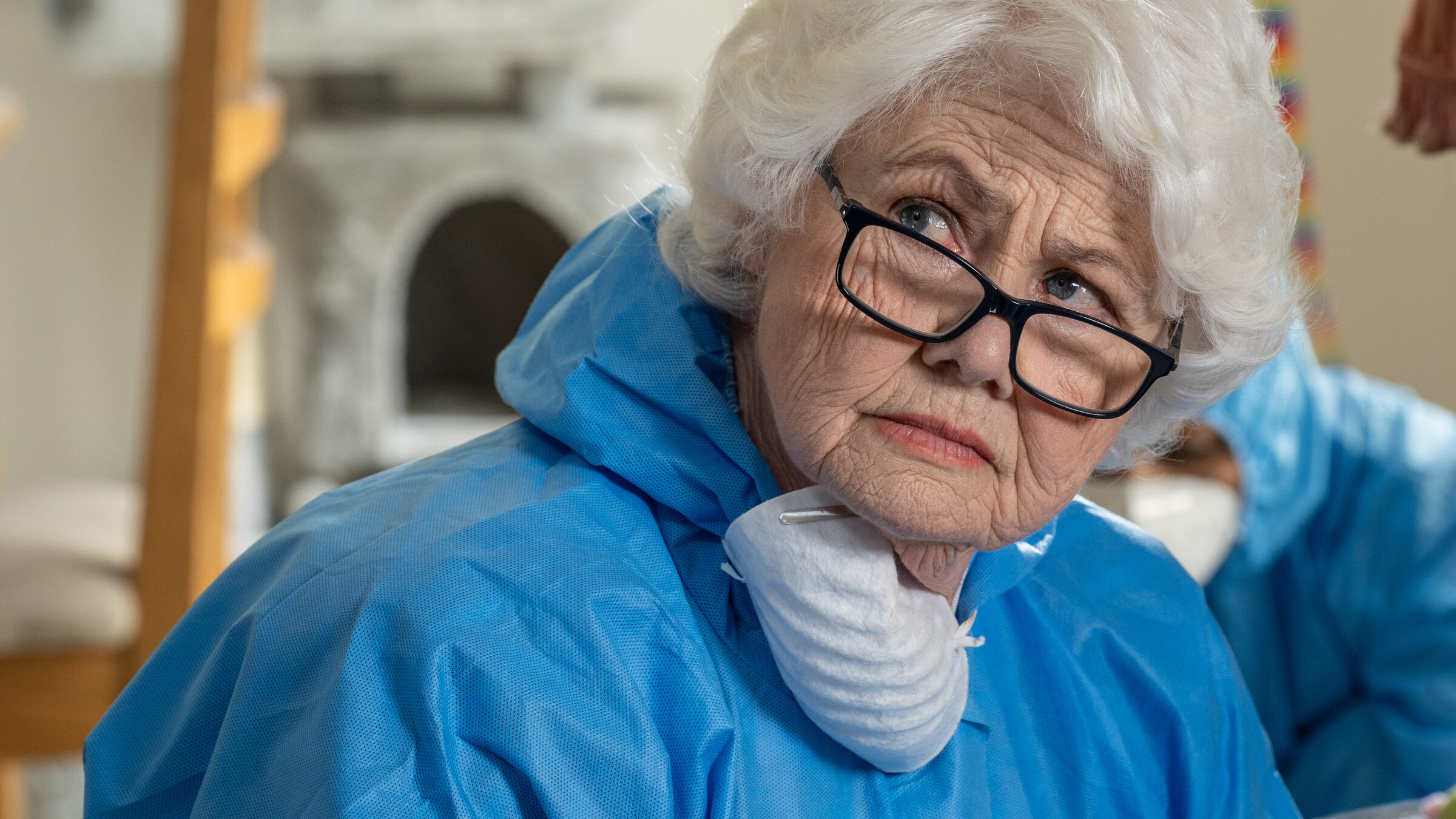 "Inspector Barnaby - Von Hunden und Menschen": Nahaufnahme: Rechtsmedizinerin Fleur Perkins (Annette Badland) trägt einen blauen Ganzkörper-Overall und eine Atemmaske um ihren Hals. Dabei blickt sie ernst nach zur Seite. Im Hintergrund beugt sich ein Forensiker (unbekannter Darsteller) nach unten.
