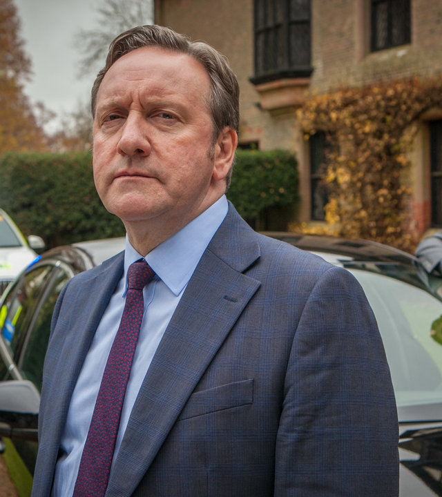 "Inspector Barnaby - Die verfluchte 9": DCI John Barnaby (Neil Dudgeon) und sein Assistent Jamie Winter (Nick Hendrix) stehen neben ihrem Wagen. Im Hintergrund parkt ein Streifenwagen.